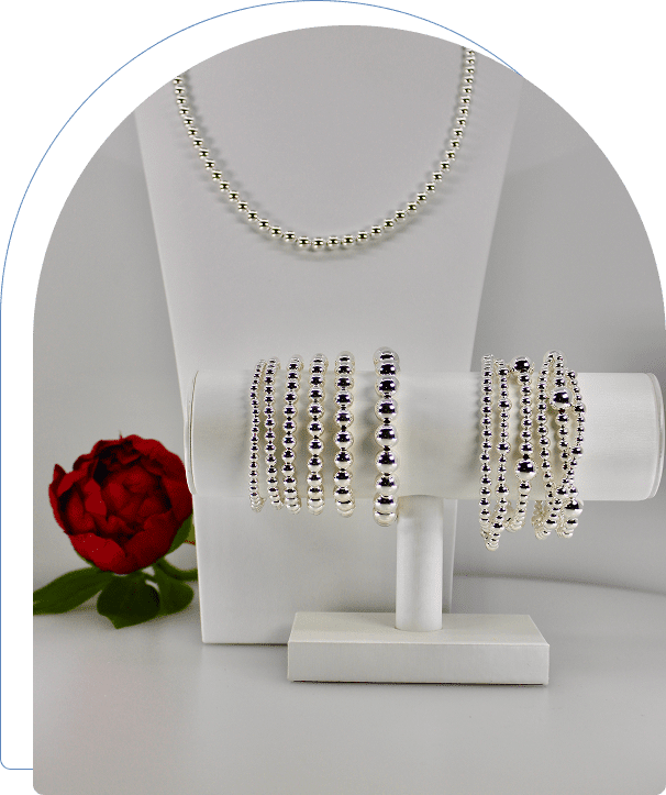 Elegant silver bangles and a pearl necklace displayed with a red rose.