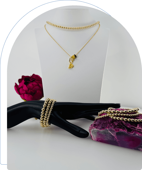 Elegant gold necklace and pearl bracelets displayed with a red rose and purple gift box.