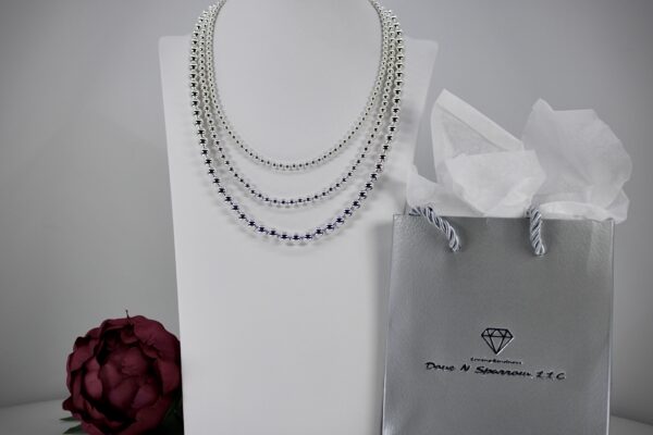 Elegant layered silver necklace displayed with a branded bag and flower.